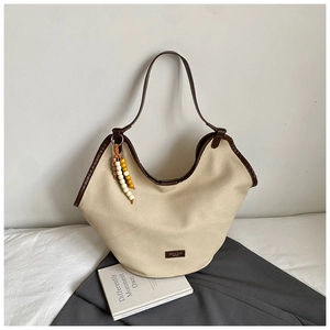 Detail view of canvas underarm bag with brown leather trim and wooden bead charm