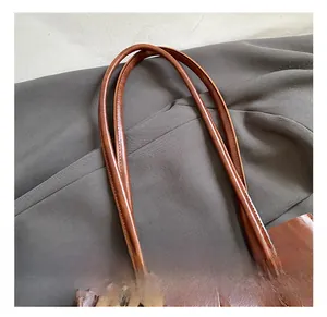 Close-up of brown faux leather tote bag showing reinforced stitching and teddy bear charm