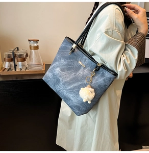 Detail of blue denim tote bag with black leather trim and white plush sheep charm