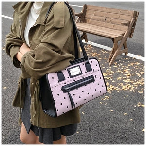 Detail of pink polka dot shoulder bag with black bow print and metal brand logo plate