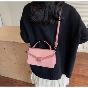 Detailed view of pink leather crossbody bag with buckle, worn over a black cardigan
