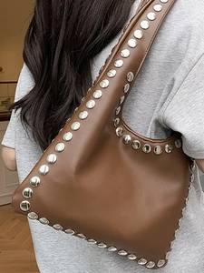 Sac hobo en cuir marron avec rivets argentés porté par un mannequin au style rétro