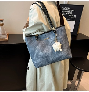 Blue denim tote bag with black leather straps and plush charm shown on a model