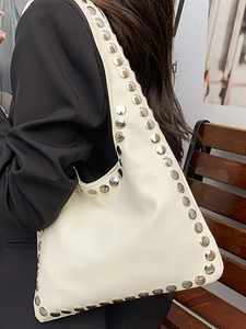 Sac fourre-tout crème chic avec rivets argentés porté sur un mannequin en blazer noir