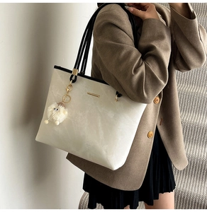 Detailed side view of cream white tote bag with gold metal trim and plush charm detail