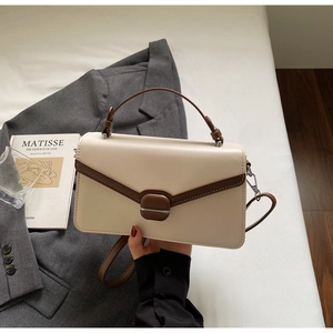 Detail of a white and brown color-block crossbody bag with V-shaped flap and magnetic closure