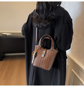 Détail du sac seau en cuir tressé marron avec cadenas et pompon en perles bois