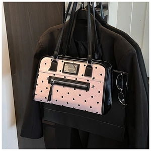 Detailed close-up of a pink polka dot tote bag with metal nameplate and black bow accents