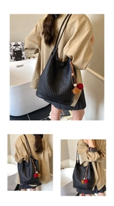 Detailed close-up of black woven texture tote bag with plush charms and dual thin straps