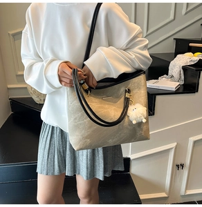 Detail of taupe suede tote bag with black straps and white fuzzy charm on a model
