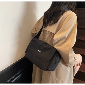 Detail of black nylon messenger bag with logo patch shown on khaki trench coat