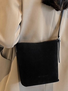 Minimalist black matte leather bucket tote bag for women worn over a beige trench coat