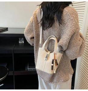 Détail du sac seau tressé avec breloque en perles et fermoir argenté porté par un mannequin