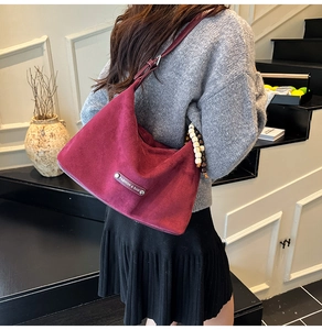 Detail view of burgundy suede hobo bag styled with a grey sweater and black pleated skirt