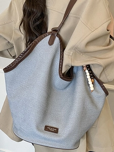 Large gray fabric tote bag with brown leather trim and beads worn by a female model