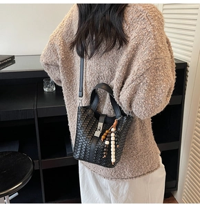 Détail du sac seau noir tressé avec bandoulière réglable et gland à franges perlées