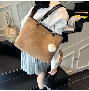 Close-up of vintage brown tote bag with black straps and white plush ball accessory