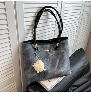 Detail of grey washed denim tote bag featuring black leather handles and sheep pendant