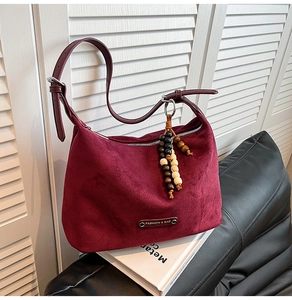 Close-up of burgundy suede tote bag with decorative wooden beads and metal fashion tag