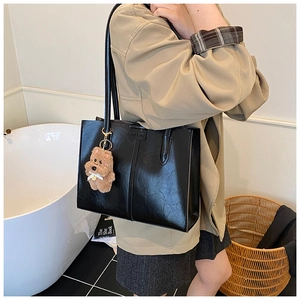 Detail view of black quilted tote bag with a brown plush dog charm and smooth PU texture