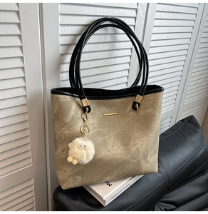 Detail of large brown tote bag with marble texture, black straps, and plush lamb charm
