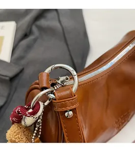 Detail of glossy brown leather handbag featuring silver hardware and a plush charm