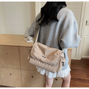 Detail of a minimalist beige nylon messenger bag with adjustable strap shown on a model