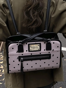 Minimalist light pink tote bag with black polka dots and gold logo plate worn by a model
