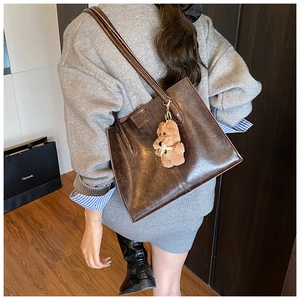 Detail of vintage dark brown tote bag in glossy oil wax leather with teddy bear charm