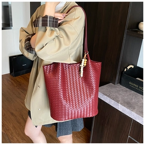 Detail of burgundy woven tote bag showing leather texture and wooden bead charm accessory