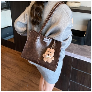 Detail view of coffee brown vintage tote bag with cute plush bear charm on shoulder