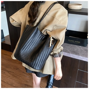 Detail of black woven tote bag featuring decorative wooden beads on a slender shoulder strap
