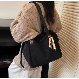 Detail of black drawstring tote bag with rustic wooden bead tassel and side pockets