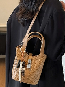 Sac seau tressé marron avec breloque perlée et bandoulière sur un modèle en blazer noir