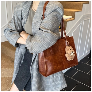 Detail view of large brown vintage tote bag with plush bear charm on a shoulder strap