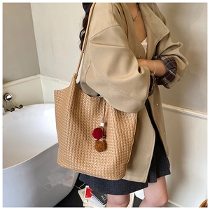 Detail of a khaki woven tote bag with a dual-color decorative pompom charm and straps