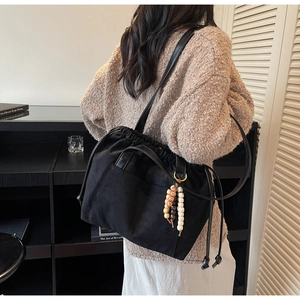 Detail view of black drawstring tote bag with decorative wooden beads on a model