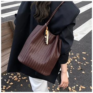 Detail of dark brown woven tote bag with wooden bead charm on a park bench