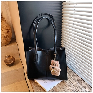 Detail of black leather tote bag featuring a cute plush animal charm and elegant straps