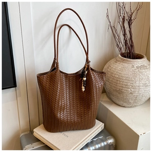 Detail of dark brown woven tote bag showing Intrecciato texture and bohemian bead tassel