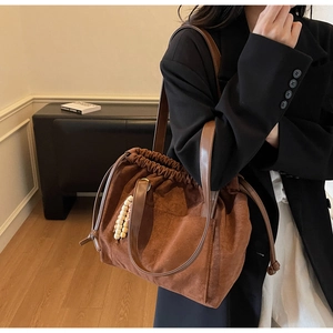 Detail of dark brown suede tote bag with drawstring closure and wooden bead charm on shoulder strap