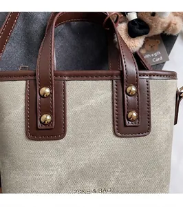 Close-up of canvas bucket bag with leather handles and gold rivet reinforcements