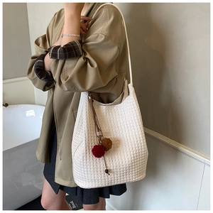 Close-up of white woven leather hobo bag with colorful plush ball charm decoration