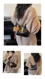 Detail of black glossy hobo bag featuring a cute plush bear pendant and striped ribbon