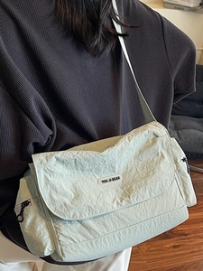 Minimalist light green nylon tote bag shown on model in a cozy interior setting
