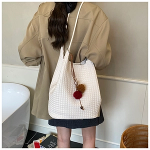 Detail of white woven texture shoulder bag with colorful plush ball charms on a model