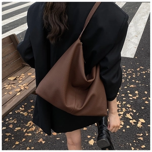 Close-up of caramel brown pebble leather hobo bag with wide shoulder strap on a park bench