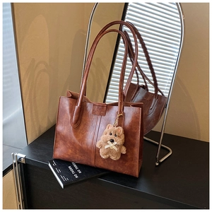 Close-up of vintage brown tote bag with oil wax texture and cute plush bear charm