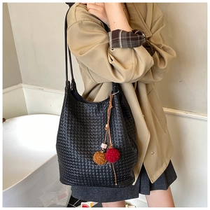 Detail of woven black tote bag with long leather strap and colorful pompom charms