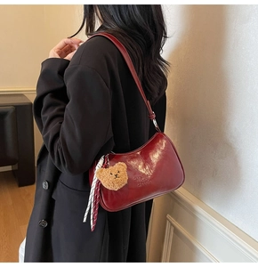 Detail of burgundy underarm bag featuring glossy texture, logo embossing, and bear charm